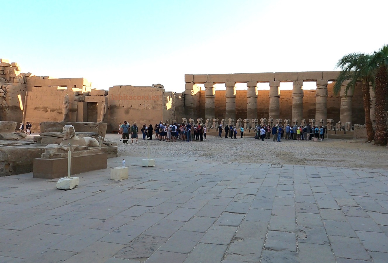 En el gran patio están la esfinge con la cara de Hatshepsut, el templo de Ramsés III y esfinges con la cabeza de carnero junto a grupos de visitantes en Karnak, Lúxor. Egipto.