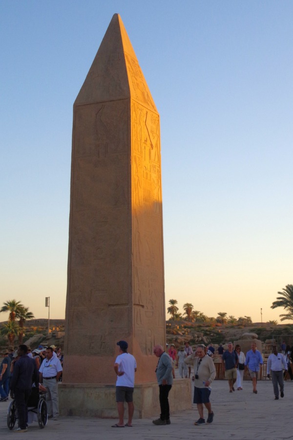 El obelisco que se rompió de Hatshepsut y detrás el dios Jepri o el Escarabeo con visitantes dándole las vueltas en Karnak, Lúxor. Egipto.